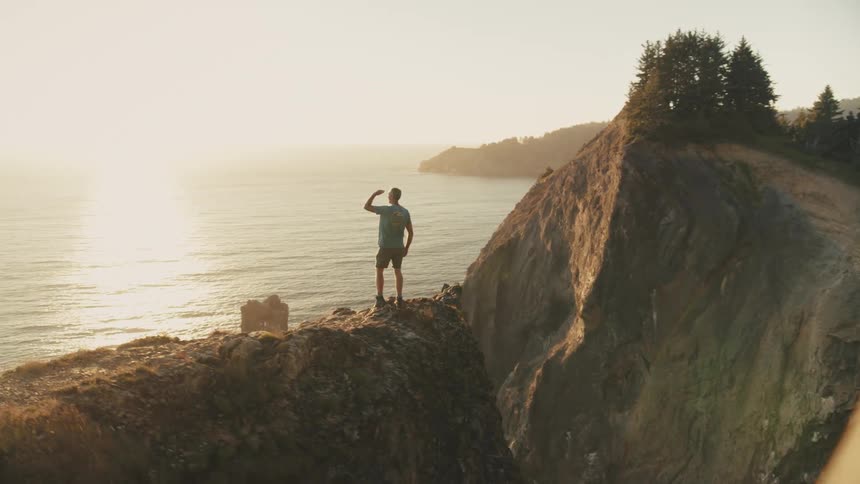 Man on a cliff with an ocean and the sun on the horizon