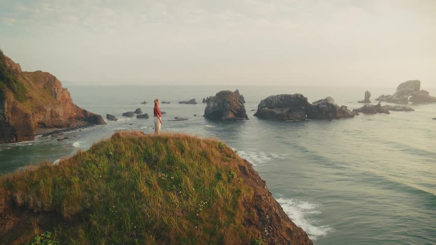 Person stands on promontory and stretches while looking at ocean landscape