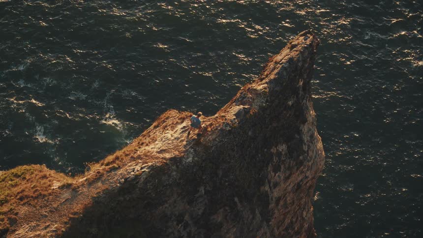 A man walking then stopping on a cliffs edge over the ocean