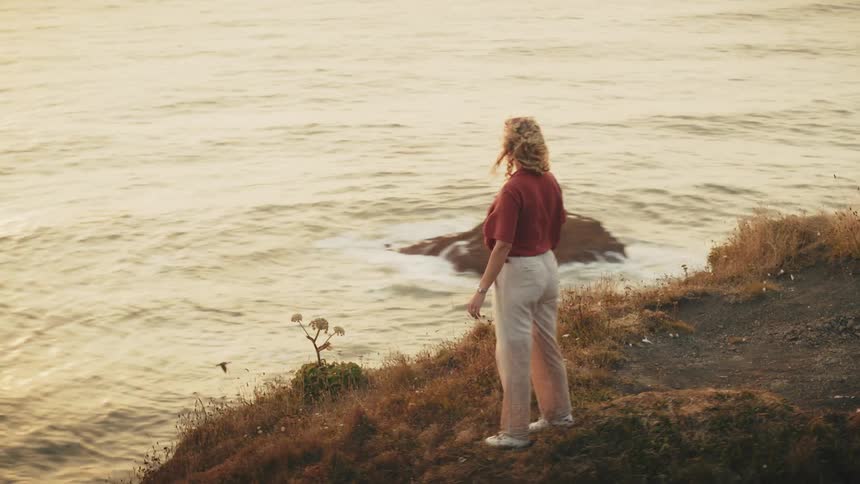 Woman spreading her arms while standing on a mountain cliff by the sea