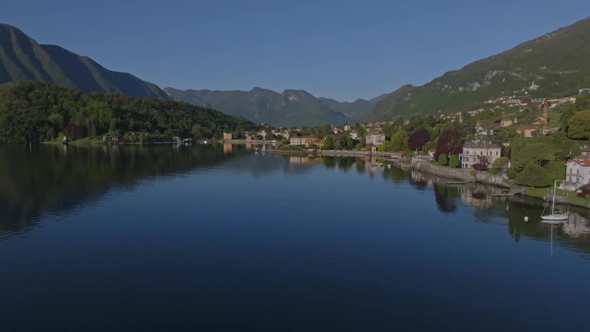 Calm lake with mountains and buildings around under a clear blue sky
