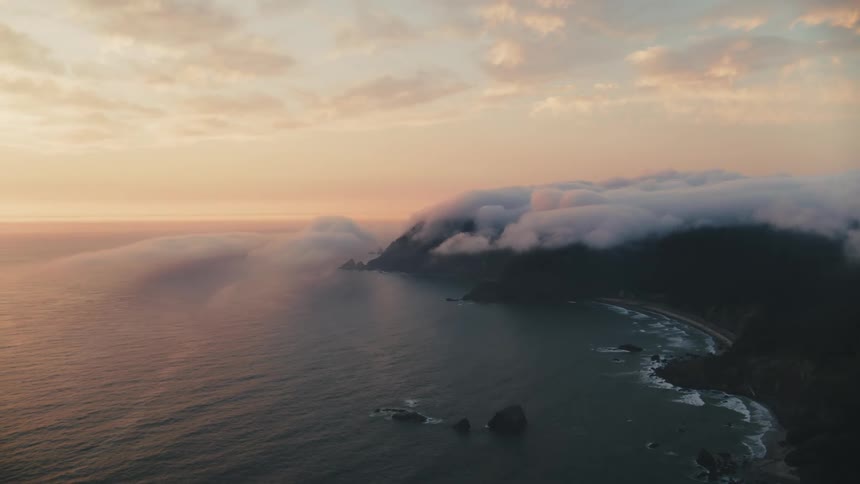 A serene coastal landscape at sunrise or sunset with lowlying clouds over a headland extending into the ocean