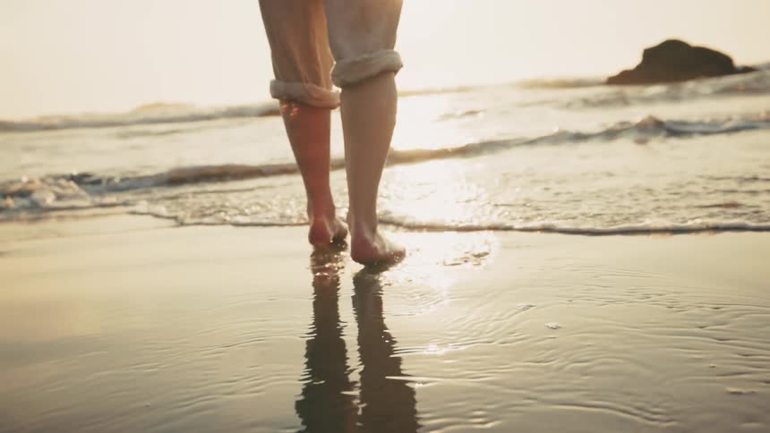 Legs of a person walking backwards on a beach one morning
