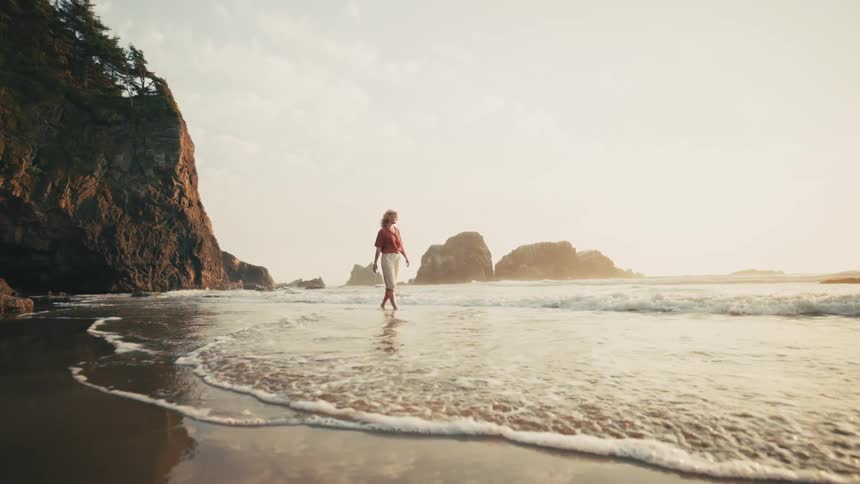 Person wades through the surf while walking away from a seaside cliff on a cloudy day
