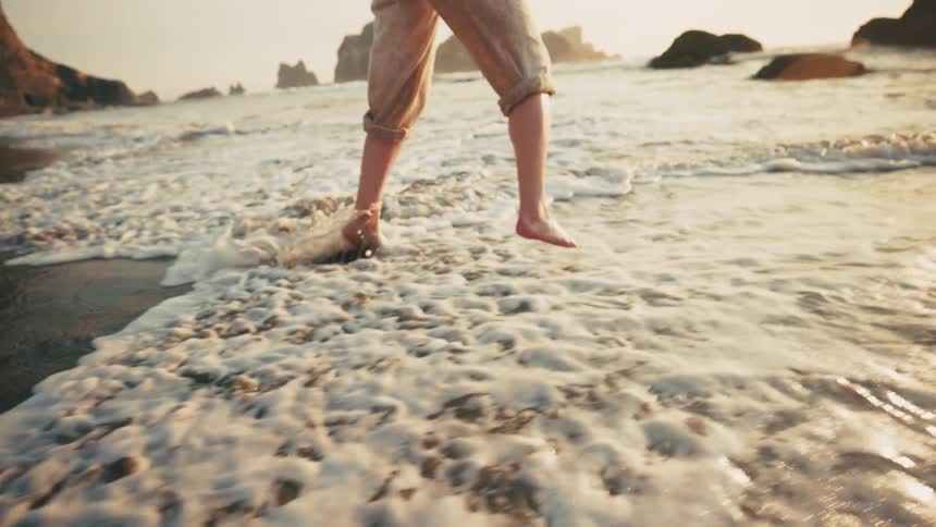 On a beach running and jumping at waters edge with rolled up pants