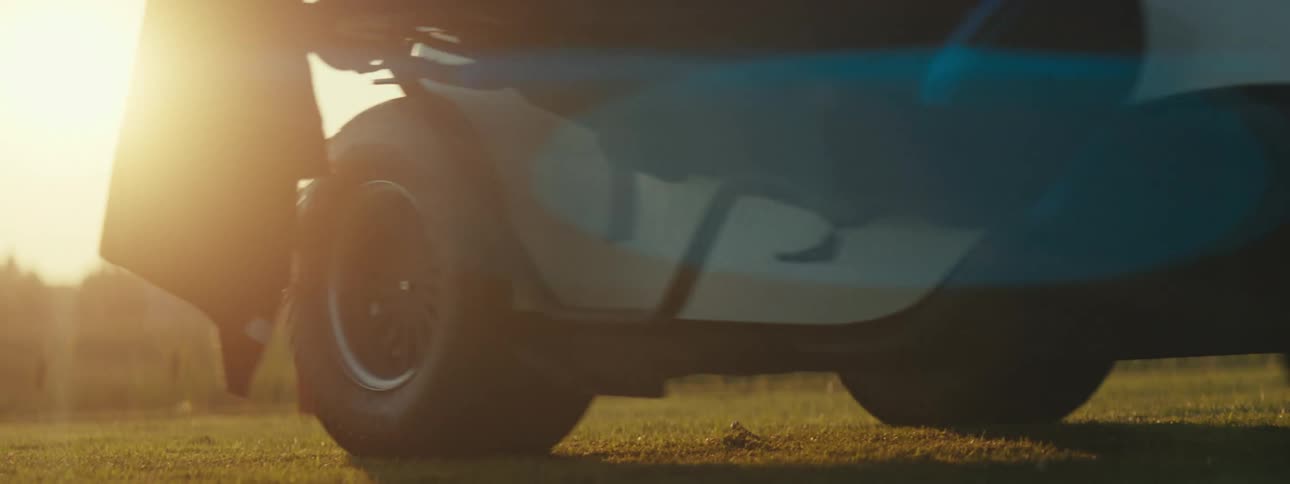 Wheels of a golf cart stopping in a grass field with the sun on the horizon