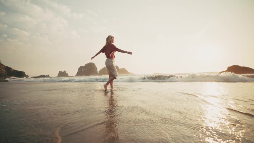 Woman walking on the beach with the sun on the horizon