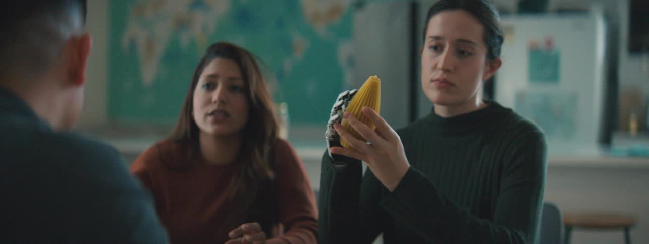 Woman with a robotic hand holding an abstract yellow object sitting next to a woman and a man