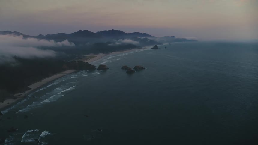 Aerial view of a coastline stretching into the distance with lush green fields under the clouds at sunset