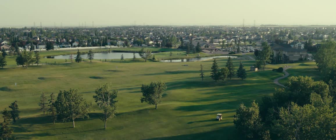 A beautiful view of a citys golf course from the sky with a cityscape visible in the distance
