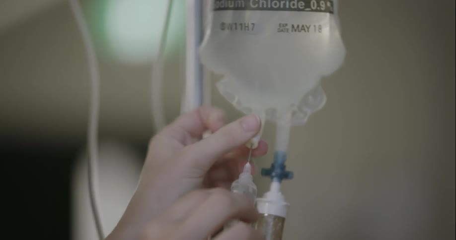 A nurse inserts a syringe into an iv bag