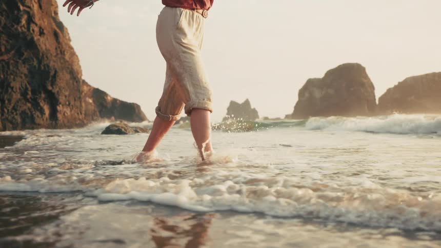 Bare feet of a woman walking on the beach with the ocean waves gently touching her feet