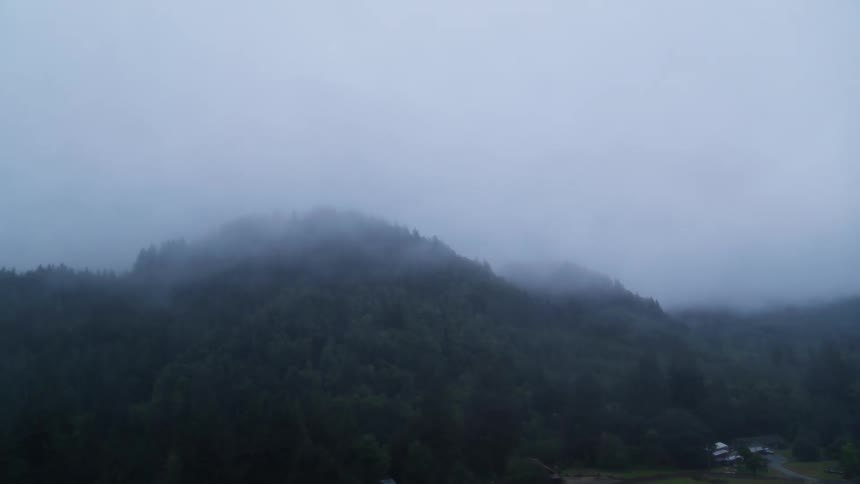 Low lying clouds obscure the tops of forested mountains surrounding rural buildings