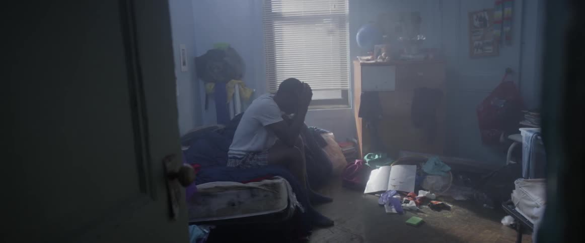 A young man in a white shirt sits up and rubs his face