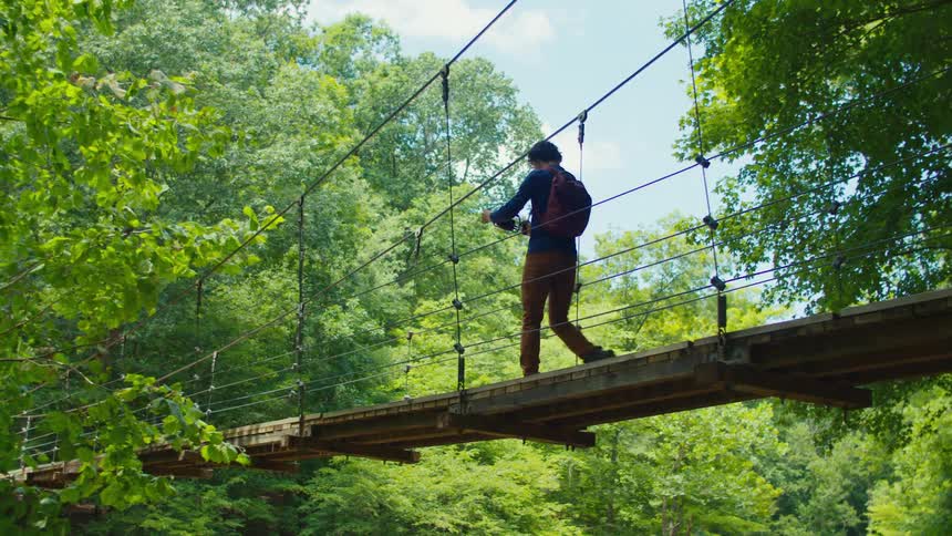 Man walking with a smartphone and a holder filming while passing through a bridge surrounded by vegetation