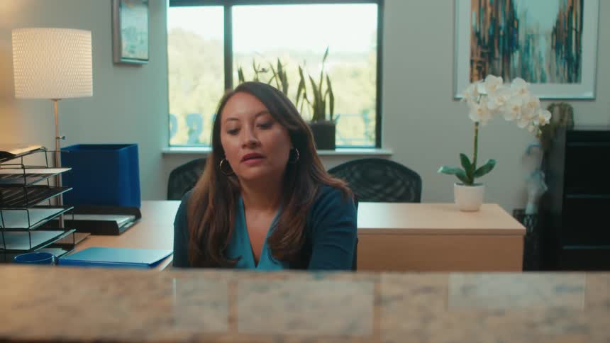A female office employee talks on the telephone while sitting at a desk