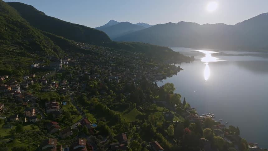 Lake waters near a small town at the base of a mountain reflect the glaring sunlight