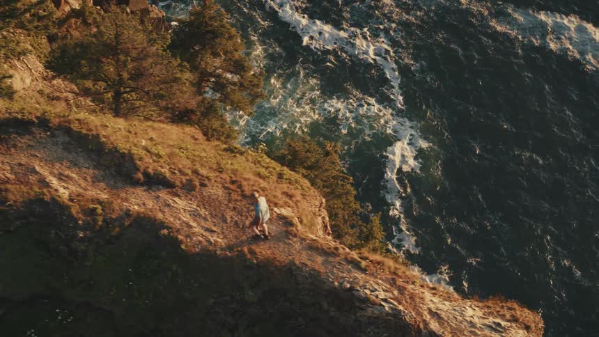 A man walks along a narrow path on the top of a mountain