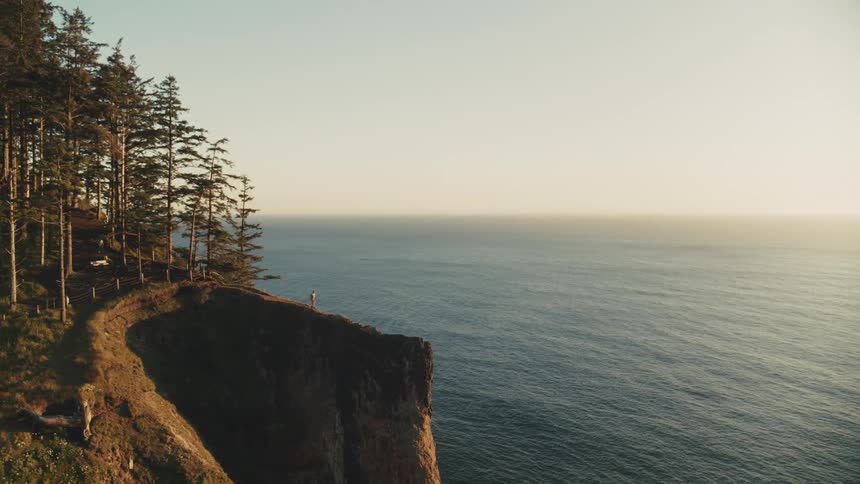 A solitary figure stands on a dramatic cliff overlooking a vast ocean