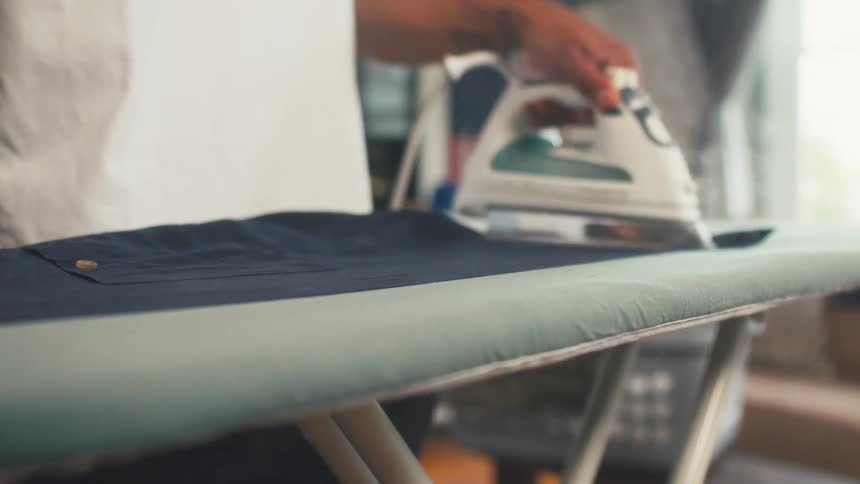 Hand of a person ironing clothes on an ironing board indoors