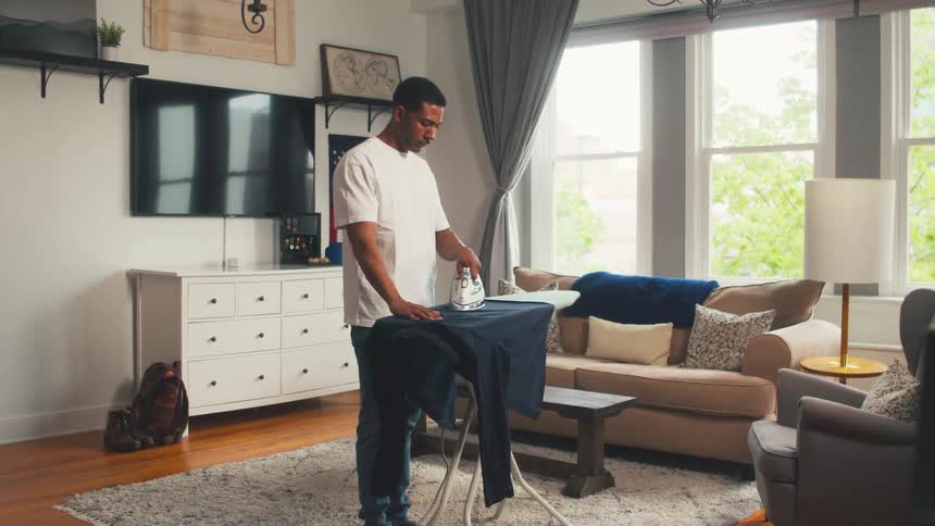A man ironing a hoodie in his living room