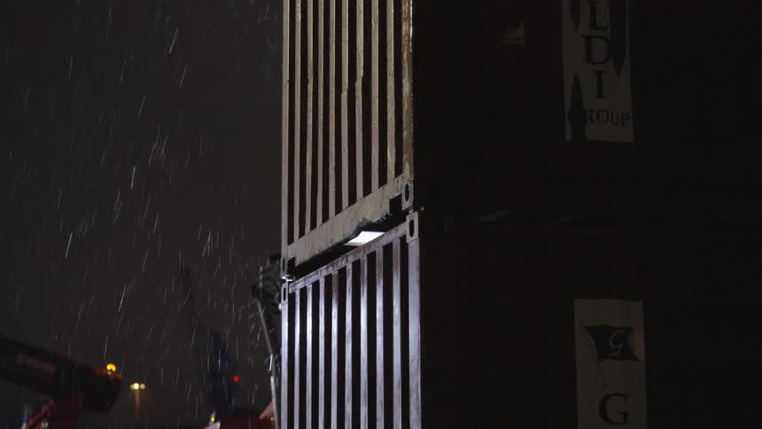 Shipping containers are being stacked in the rain at night