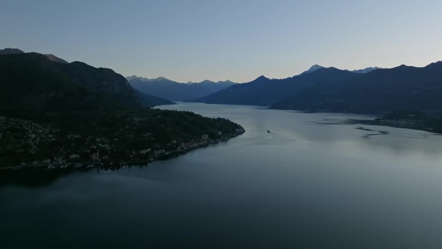 An aerial view of a boat traveling on a serene lake surrounded by mountains during twilight