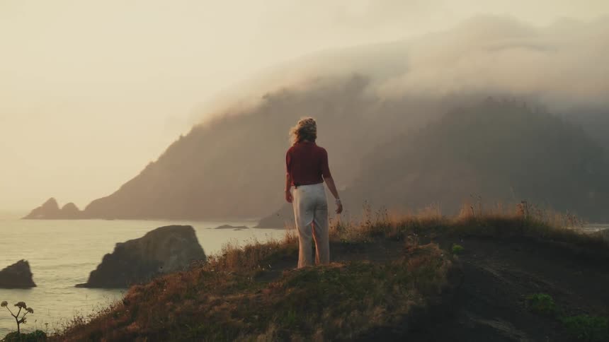 Woman on top of a hill with her arms open by the sea