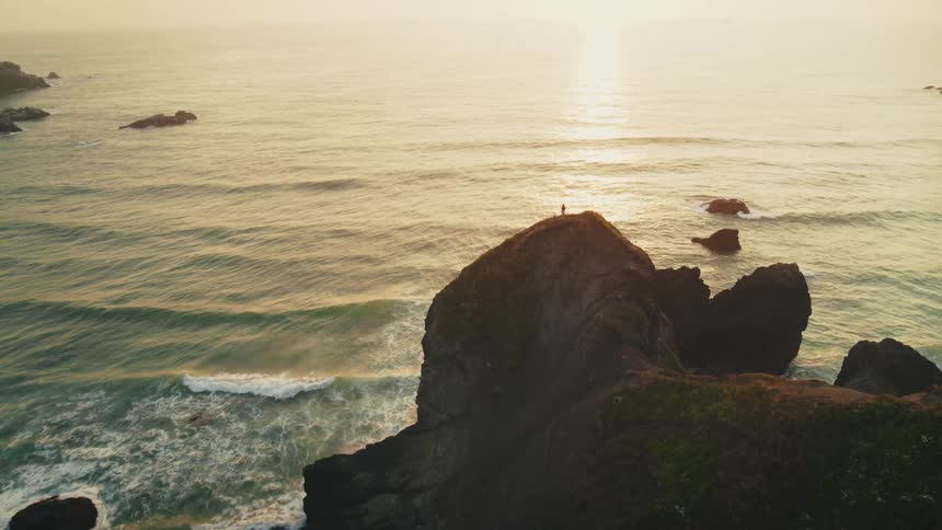 A person is standing on a large rock on the shore