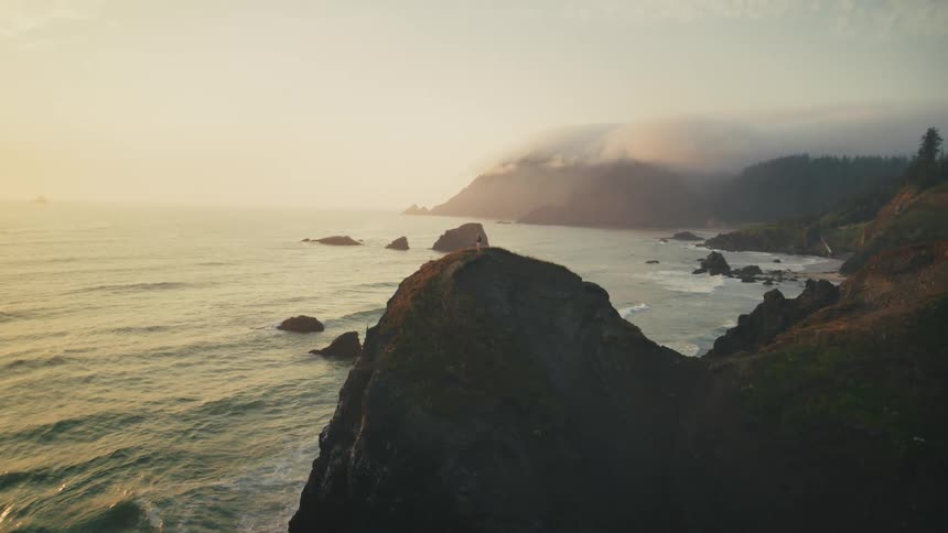 A solitary figure stands on a rocky promontory overlooking a vast ocean