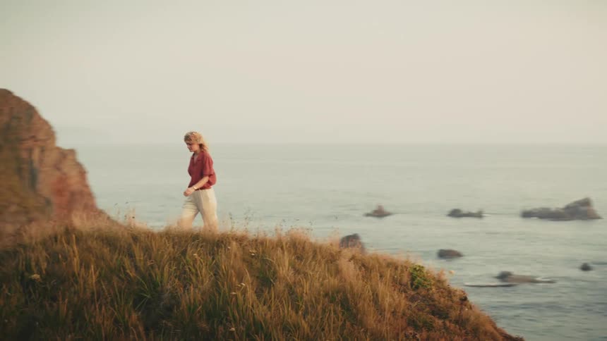 A woman walks away from the cliff on the shore