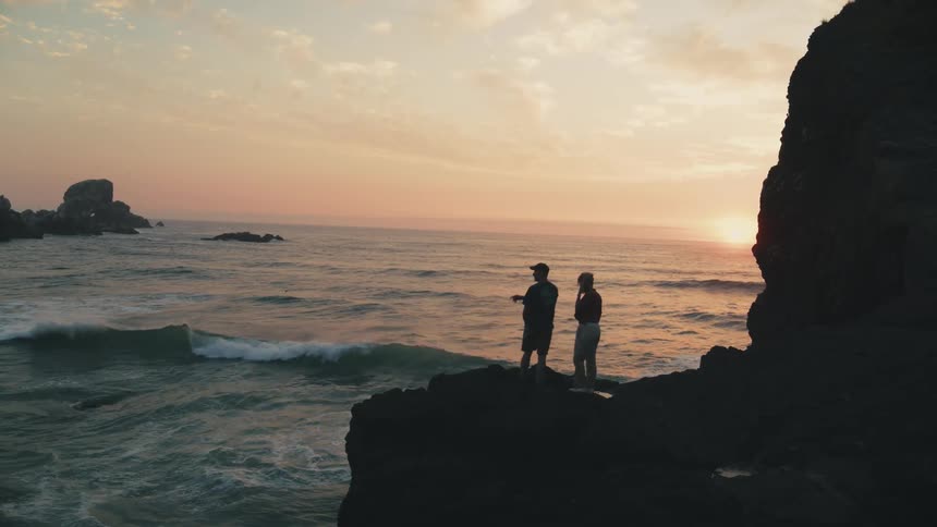 Two people silhouetted against a vast ocean at sunset