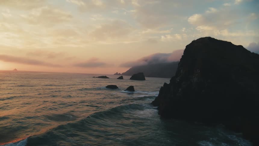 A coastal landscape at sunset with waves washing against rocky shores