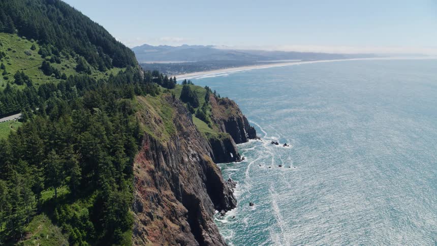 Rugged cliffs overlooking a vast ocean and a distant mountain range on the horizon under a blue sky