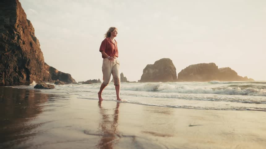 A woman walking barefoot along a beach at sunset