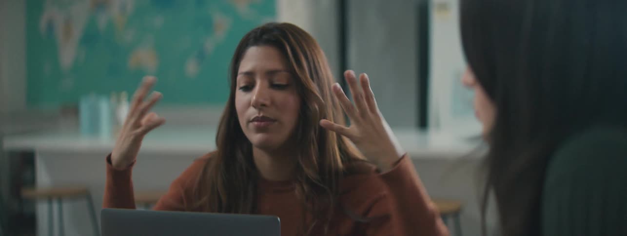 Two women sitting talking with one of them in front of a laptop
