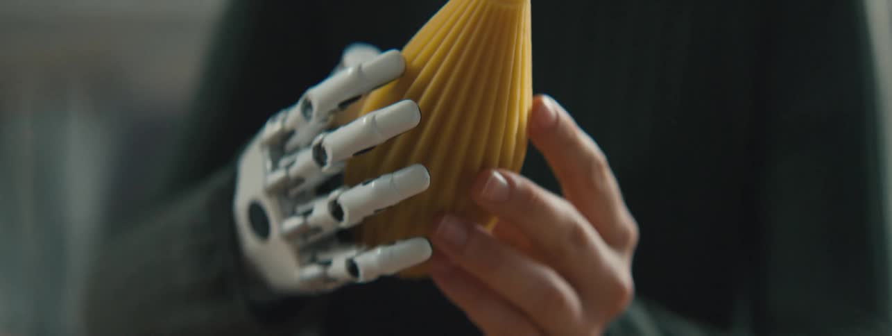 A woman with a mechanical prosthesis for a hand holds and inspects an oval 3d printed object