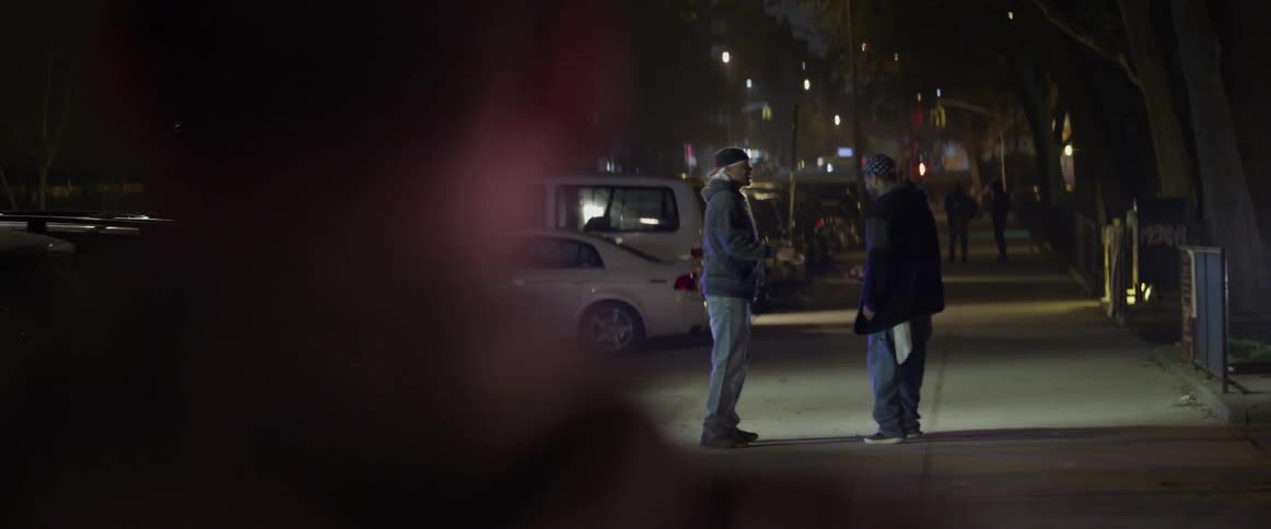 A person watches two men make a drug deal in the city at night