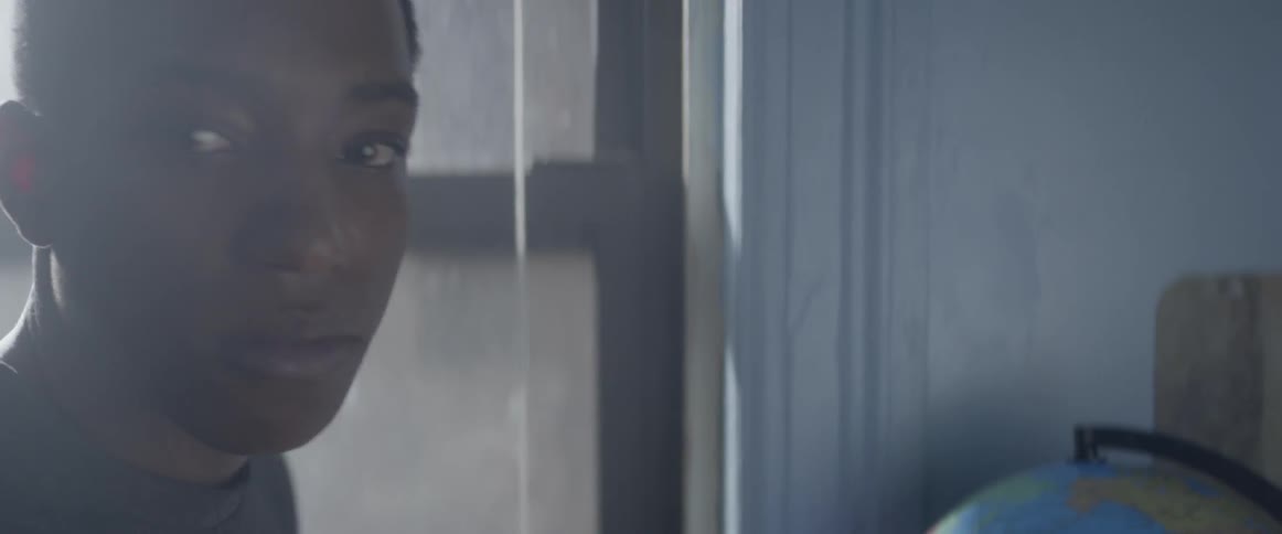 A boy who is looking out the window turns towards the camera