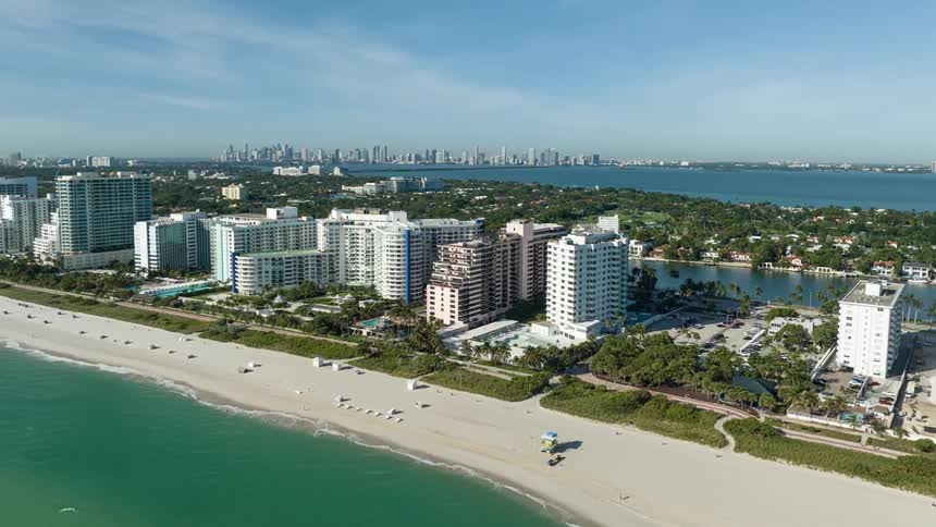 An aerial view of a coastal cityscape with a long stretch of white sandy beach high rise buildings lining the shore and a distant skyline in the background