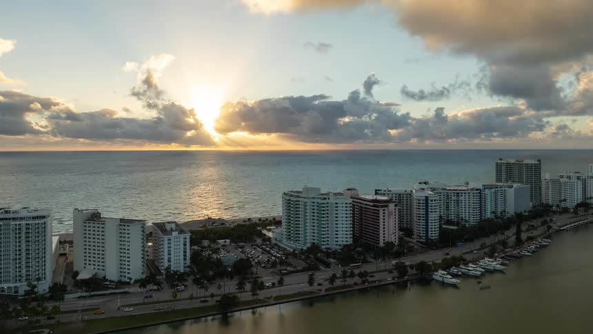 An aerial view captures the sunset over a coastal cityscape with numerous high rise buildings lining the shoreline