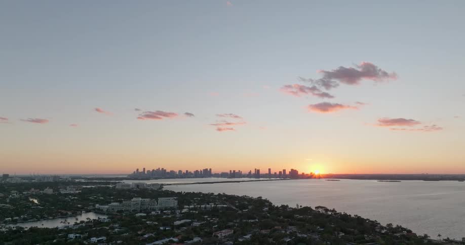 An aerial view of a large city with tall buildings on the horizon and in front of it a large amount of water on a morning