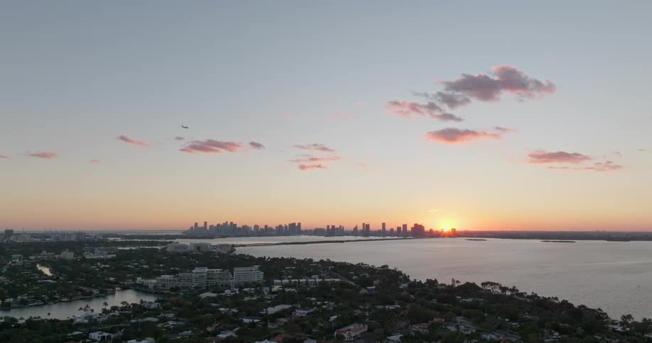 A view of a huge metropolitan city on the horizon that is behind a large body of water and with the sun appearing in the morning
