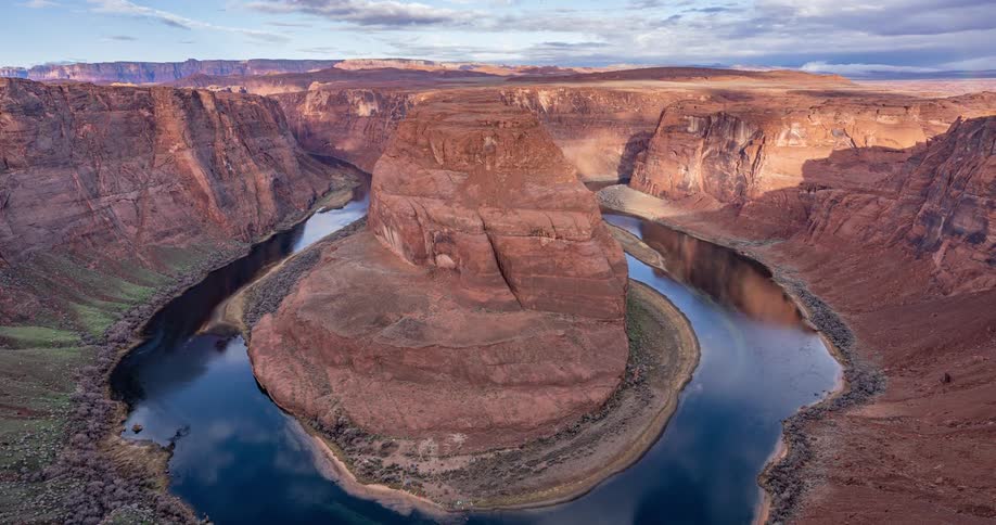 An aerial view captures the iconic horseshoe bend the colorado river winding through a deep canyon with rock formations and a blue sky