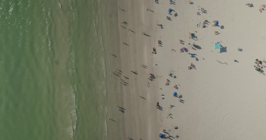 An aerial view of a beach with people on the sand on the right side and on the left side the sea water with small waves breaking
