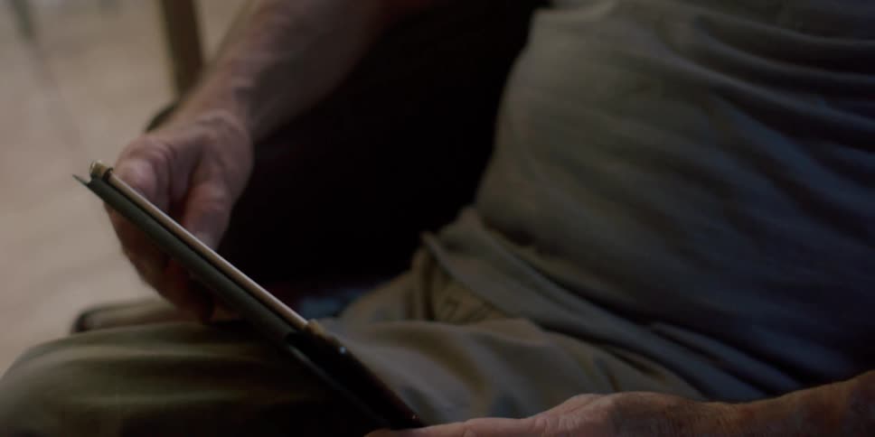 A man laughs as he looks at his tablet