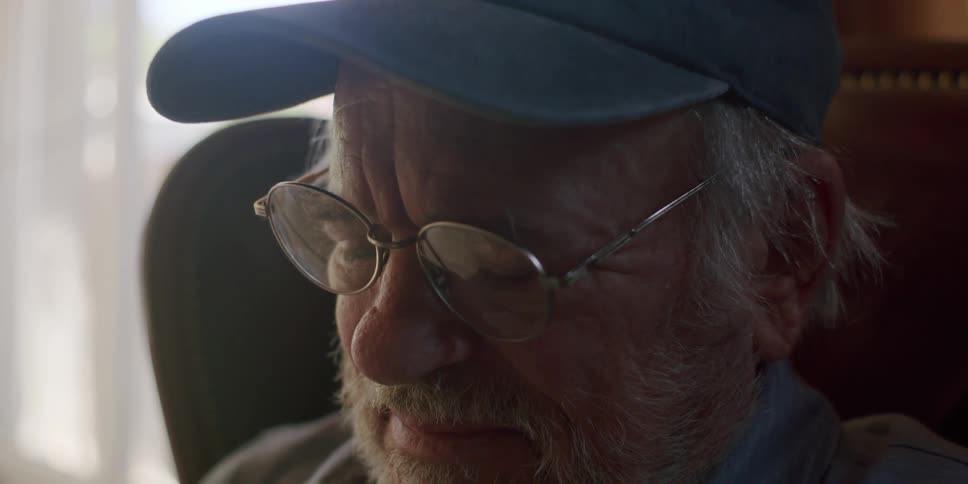 Elderly man with glasses and a cap sitting in an armchair laughing