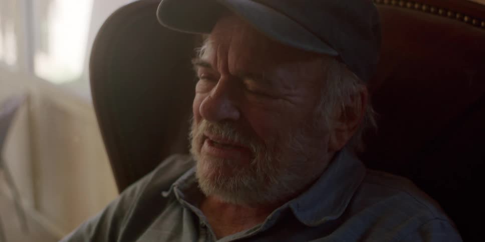Elderly man sitting in an armchair interacting with a tablet and taking off his glasses with a happy facial expression