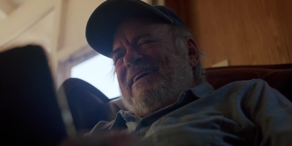 Elderly man sitting in an armchair laughing and taking off his glasses