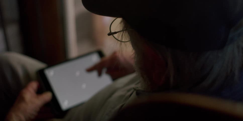An elderly man wearing a hat and glasses uses a tablet